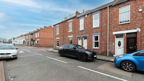 A residential street with terraced houses, a black car parked on the side, and a blue car parked in front of a house. - Modern 2 Bed Near Seafront and Easy Commute Links (South Shields)