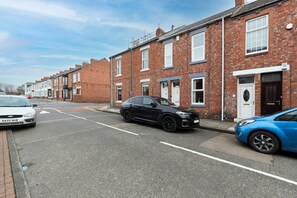 A residential street with terraced houses, a black car parked on the side, and a blue car parked in front of a house. - Modern 2 Bed Near Seafront and Easy Commute Links (South Shields)
