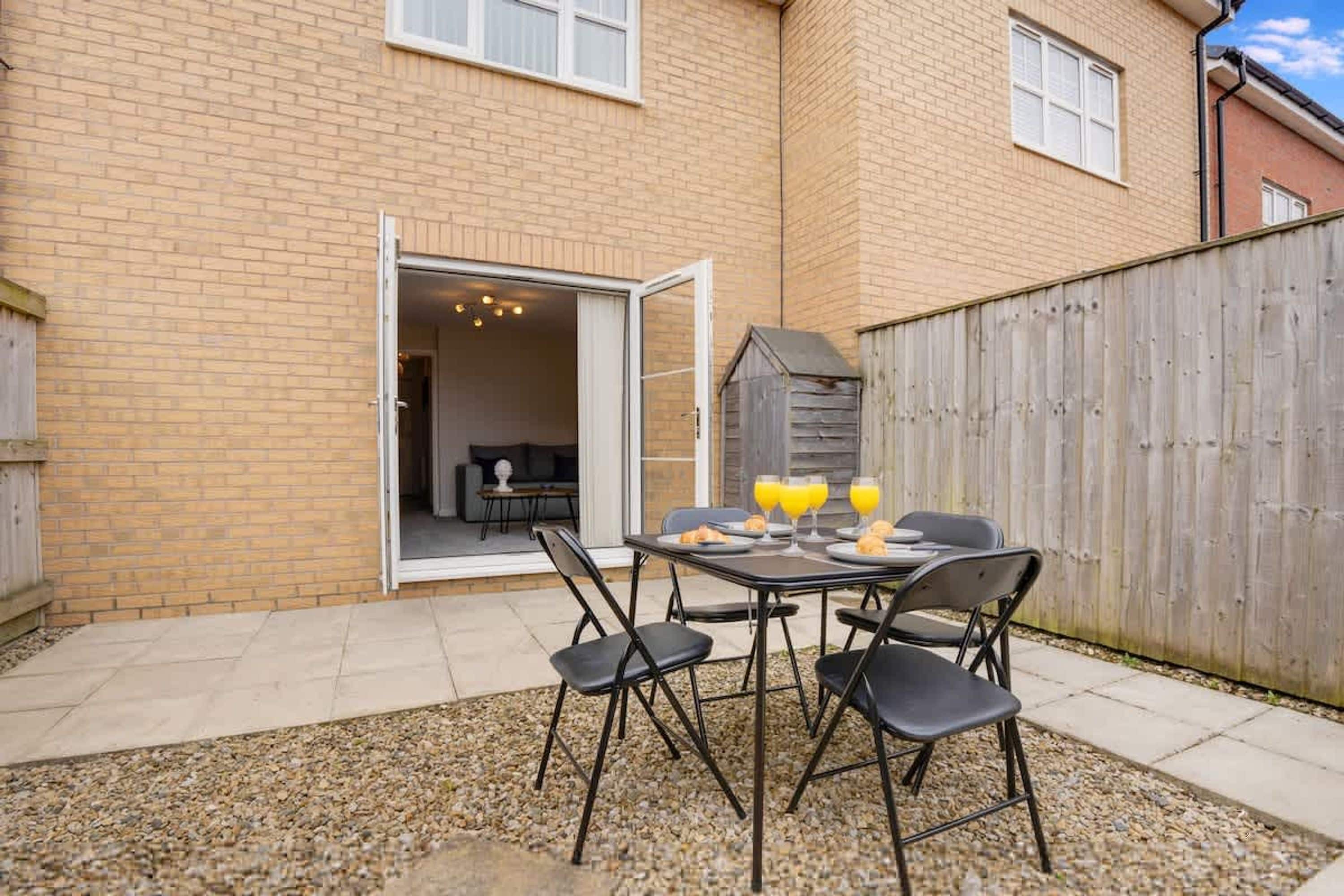 Une terrasse avec une table et des chaises, une clôture en bois et l’entrée d’un bâtiment.