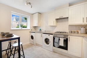 A compact kitchen with a washing machine, a stove, and a window. - Stockton 2BR Retreat Sleeps 6 Stay With Us (Stockton-on-Tees)