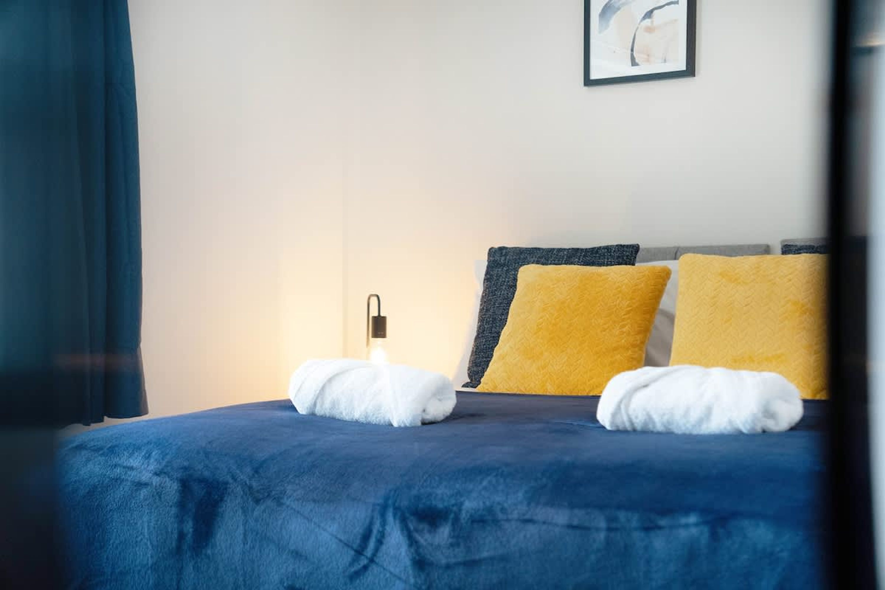 A neatly made bed with two pillows, a bedside lamp, and a wall-mounted light fixture.