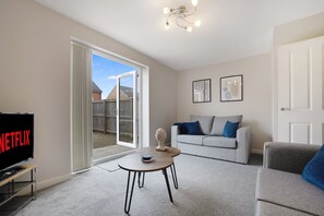 Un salon comprenant un canapé, une table basse, un téléviseur et une porte donnant sur un balcon.