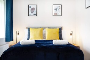 A hotel room with a large bed, two bedside lamps, and two framed pictures on the wall. - Stockton 2BR Retreat Sleeps 6 Stay With Us (Stockton-on-Tees)