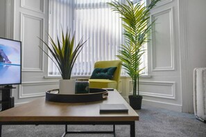 A room with a wooden table, a television, a yellow chair, and two potted plants. - 4 Bed With Easy Access to City Centre Free Wifi (Sunderland)