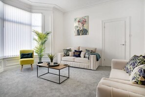 Ein Wohnzimmer mit einem gelben Sessel, einem weißen Sofa, einem Couchtisch und einem großen Fenster mit Jalousien.