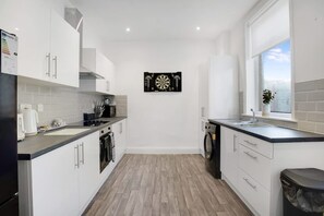 A modern kitchen with white cabinets, a black countertop, and a dartboard on the wall. - 4 Bed With Easy Access to City Centre Free Wifi (Sunderland)