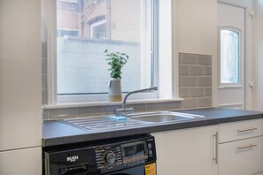 A kitchen with a built-in dishwasher, a window with a view of buildings, and a potted plant on the windowsill.