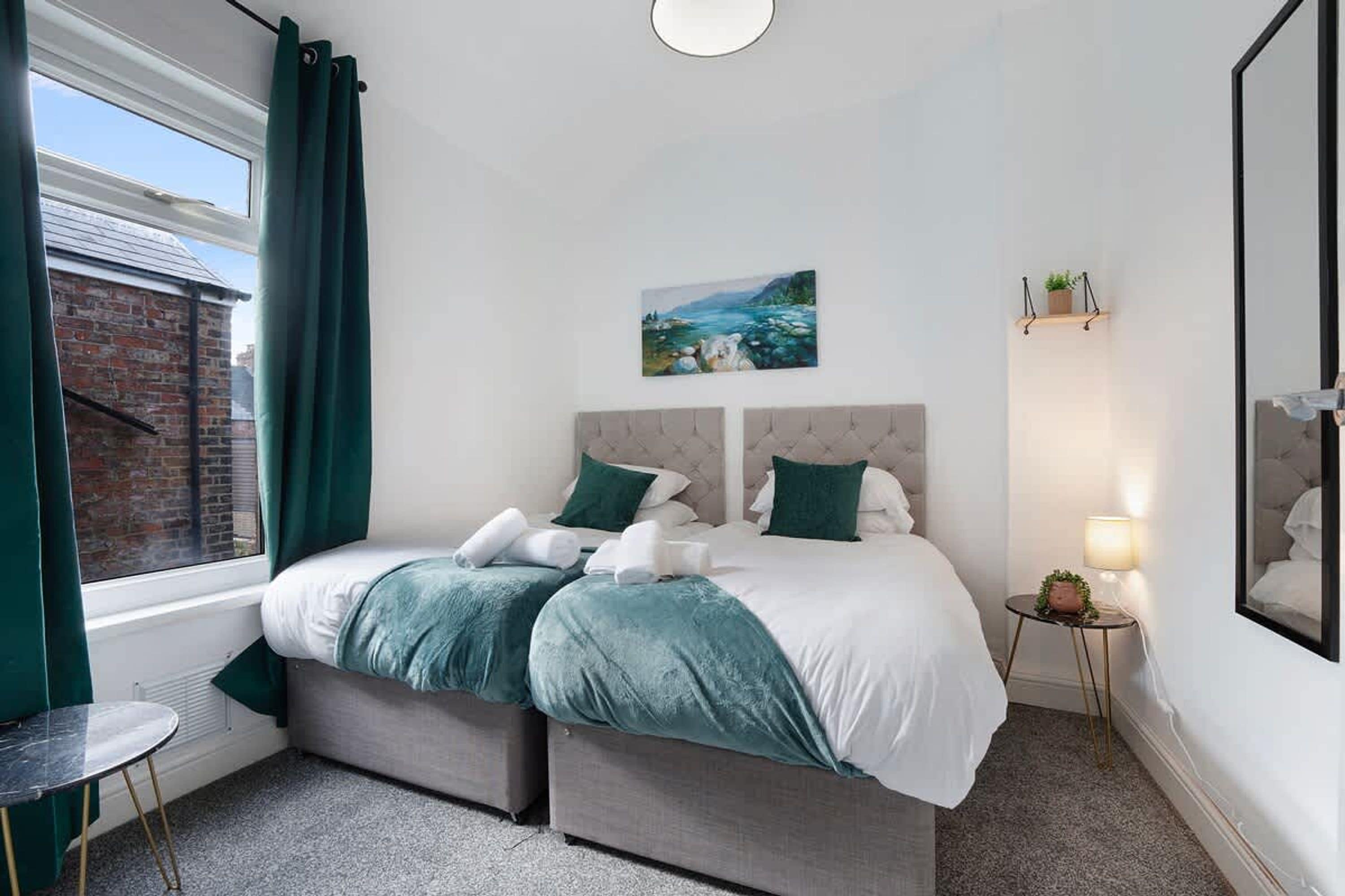 A bedroom with a bed, a painting, a bedside table, and a window with curtains.