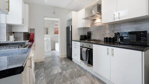 A modern kitchen with white cabinets, a black countertop, and a stainless steel range hood. - Classic 4 Bedroom Retreat Close to Infinity Bridge (Stockton-on-Tees)