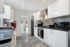 A modern kitchen with white cabinets, a black countertop, and a stainless steel range hood. - Classic 4 Bedroom Retreat Close to Infinity Bridge (Stockton-on-Tees)