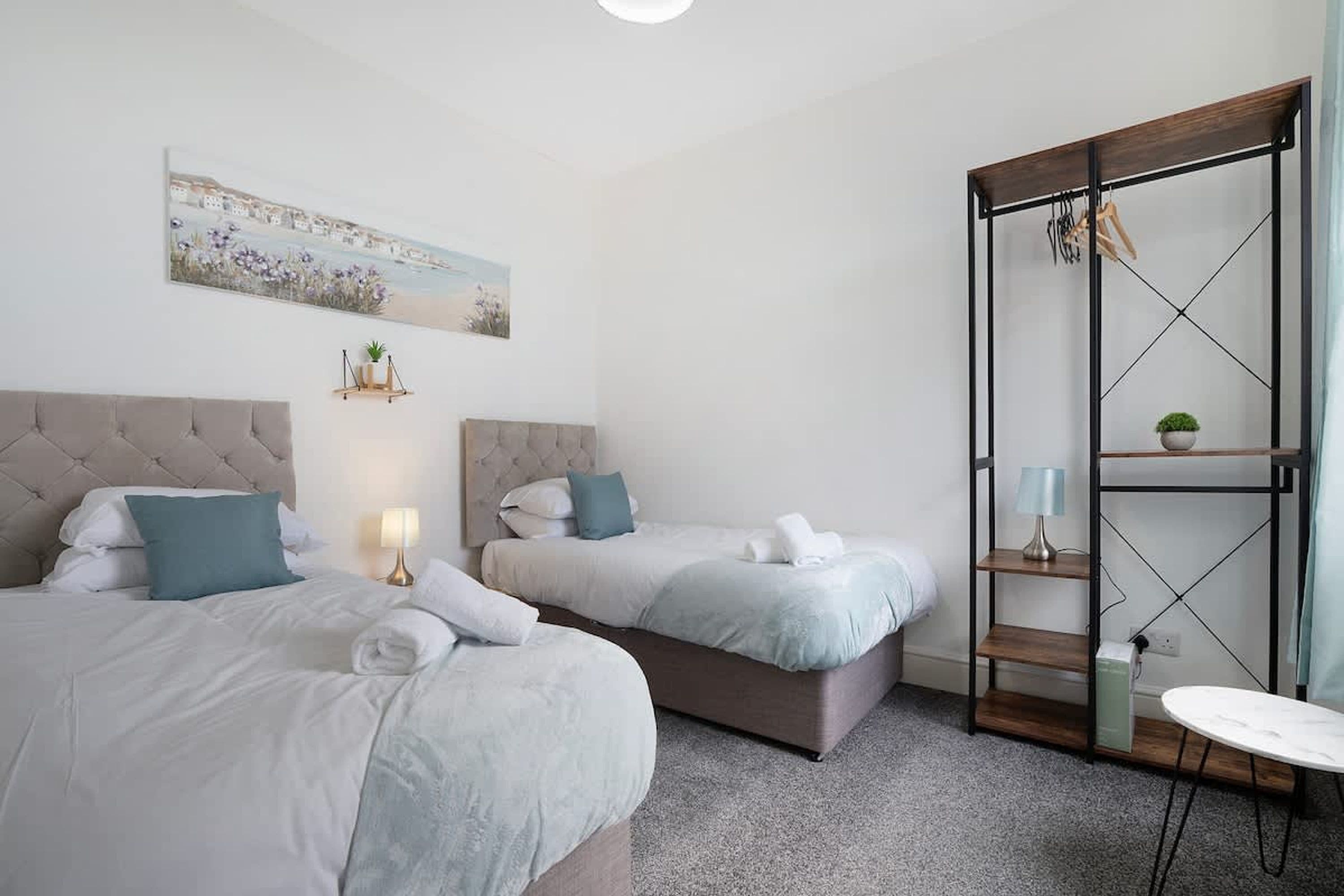 A hotel room with two beds, a painting, a small plant, and a wooden shelf with a lamp.