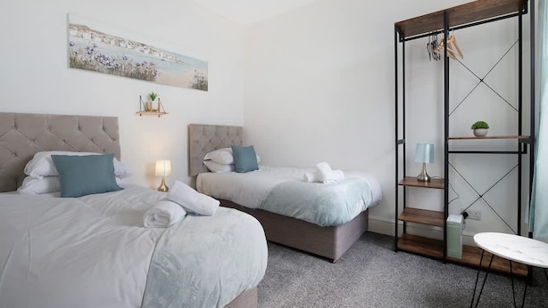 A hotel room with two beds, a painting, a small plant, and a wooden shelf with a lamp. - Classic 4 Bedroom Retreat Close to Infinity Bridge (Stockton-on-Tees)