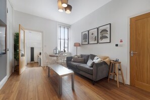 Un salon moderne avec un canapé gris, une table basse en bois et un coin repas avec des chaises blanches.