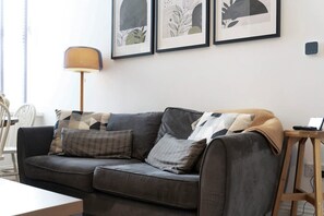 A living room with a grey sofa, patterned cushions, a floor lamp, and framed artwork on the wall. - Central Newcastle 2BR With Free Parking and Wifi (Newcastle-upon-Tyne)