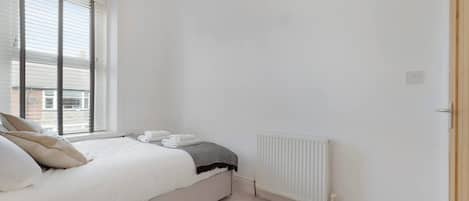 A bedroom with a bed, a radiator, and a window with blinds.