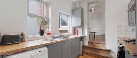 A modern kitchen with grey cabinets, a built-in washing machine, and a wooden countertop.