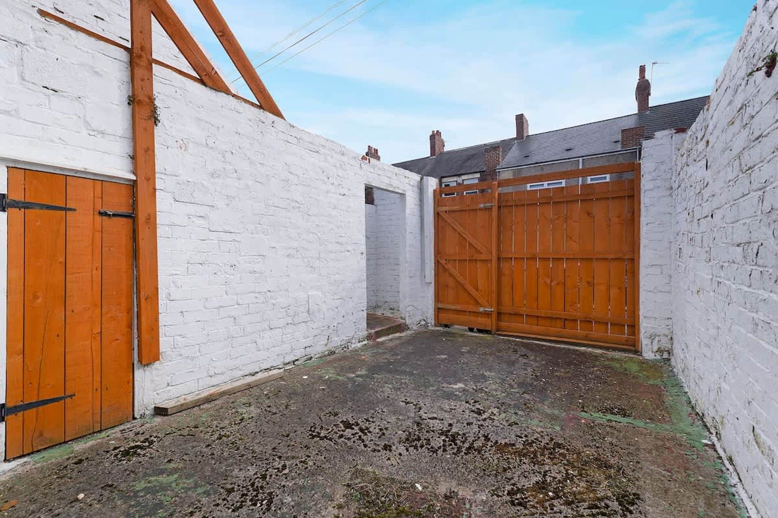 A narrow alleyway with white brick walls and wooden doors.