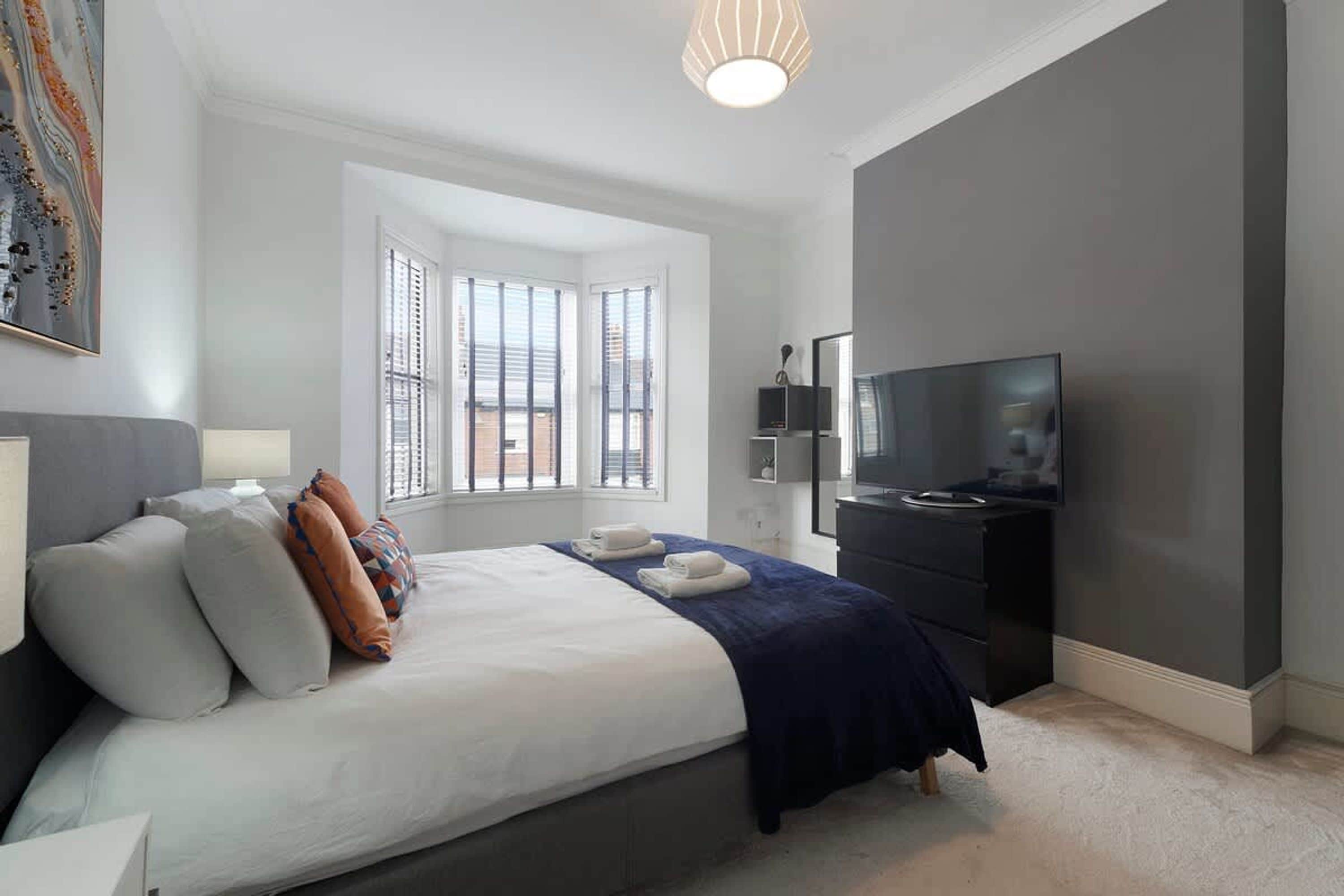 A modern bedroom with a large bed, a flat-screen TV, and a window with blinds.