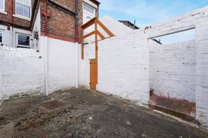 A narrow alleyway with a white brick wall, a wooden door, and a metal gate. - Central Newcastle 2BR With Free Parking and Wifi (Newcastle-upon-Tyne)