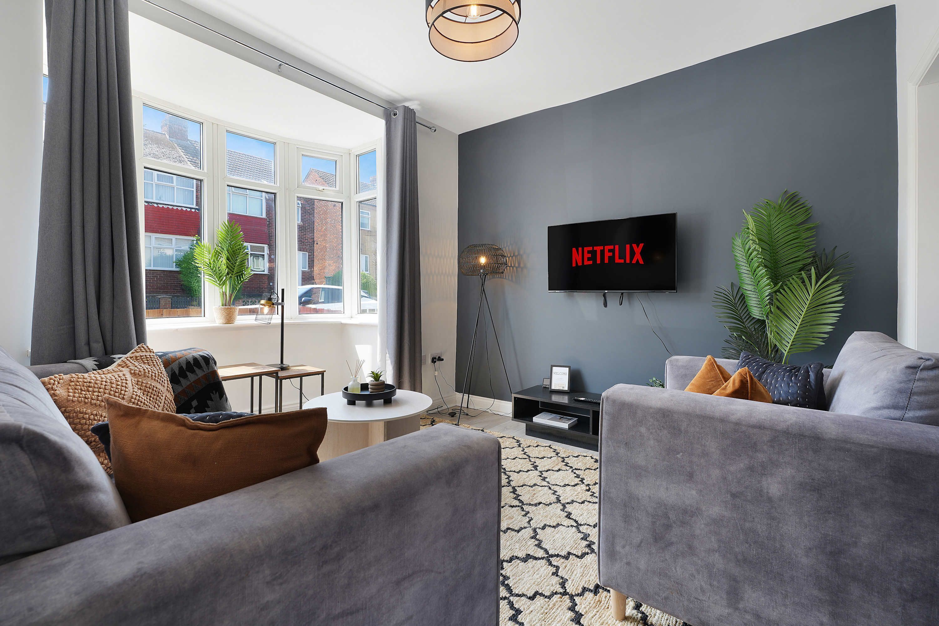 A modern living room with grey sofas, a coffee table, and a flat-screen TV mounted on the wall.