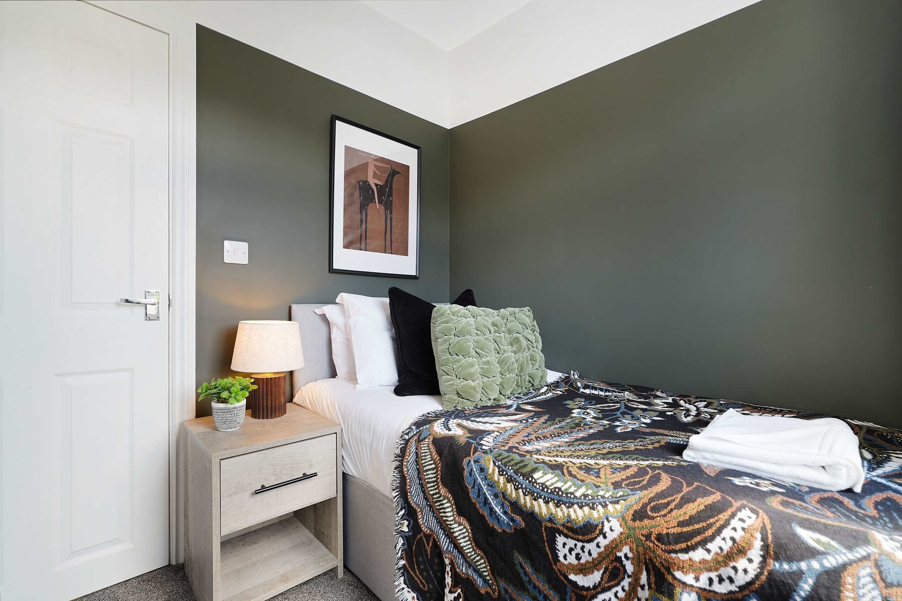 A bedroom with a bed, bedside table, lamp, and a framed picture on the wall.
