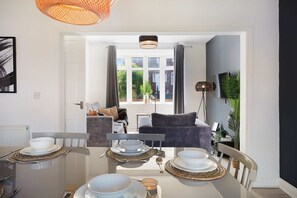 A modern dining area with a glass table, white plates, and cutlery. - Stylish Hartlepool 3BR Sleeps 5 by Stay With Us (Stockton-on-Tees)