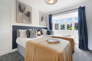 Ein Hotelzimmer mit zwei Betten, einem großen Fenster mit Vorhängen und Bildern an den Wänden.