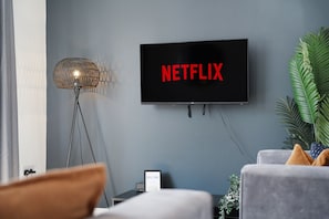 Un salon avec un téléviseur à écran plat fixé au mur, sur lequel apparaît le logo de Netflix.