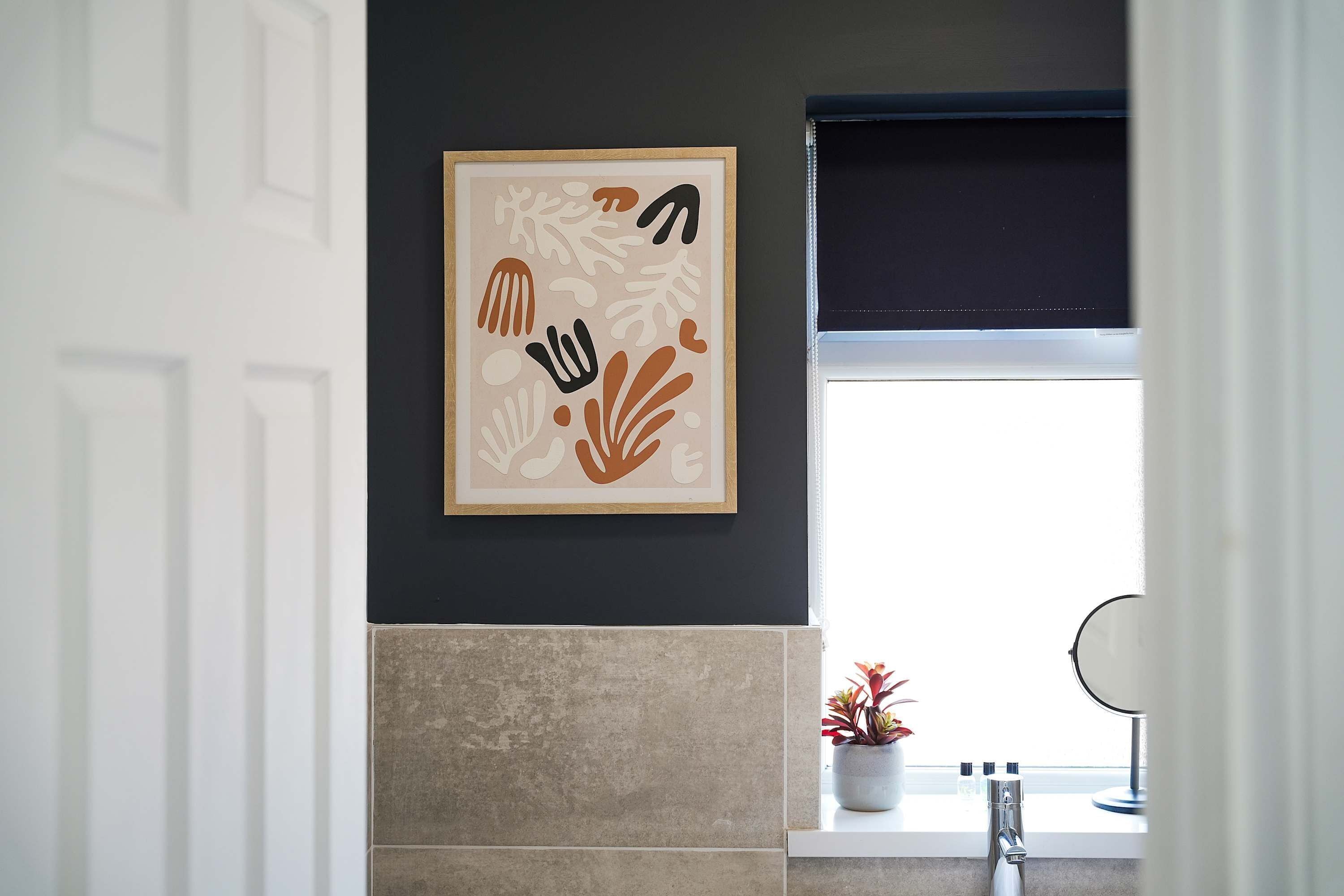 A bathroom with a framed abstract artwork on the wall, a window with a view, and a sink with a mirror.