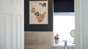 A bathroom with a framed abstract artwork on the wall, a window with a view, and a sink with a mirror. - Stylish Hartlepool 3BR Sleeps 5 by Stay With Us (Stockton-on-Tees)
