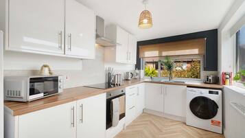 A modern kitchen with white cabinetry, a built-in oven, a microwave, a washing machine, and a window with a view of greenery.