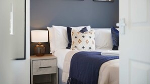 A bedroom with a bed, a bedside table with a lamp, a nightstand, and two wall-mounted mirrors. - Stylish Hartlepool 3BR Sleeps 5 by Stay With Us (Stockton-on-Tees)