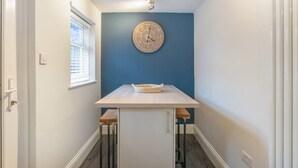 Ein schmaler Flur mit blauer Akzentwand, einer Holz-Pendeluhr und einem kleinen Tisch mit zwei Hocker.