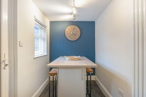 A narrow hallway with a blue accent wall, a wooden clock, and a small table with two stools. - Stylish 2 Bedroom in Bishop Auckland With Parking (Bishop Auckland)