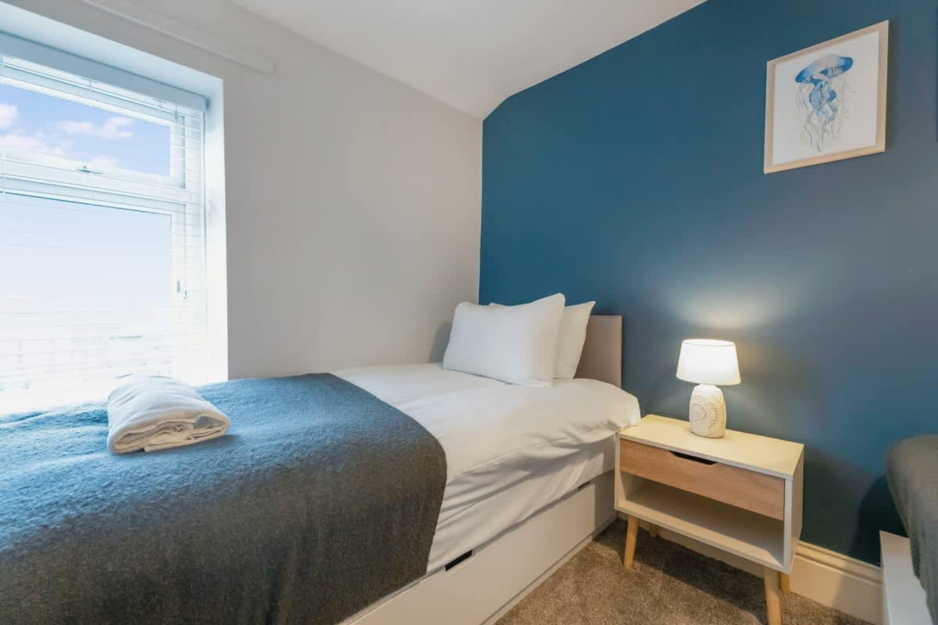 Habitación de hotel con una cama, una mesita de noche, una lámpara y una ventana.