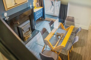 Un comedor con una mesa y sillas de vidrio, un aparador azul y una chimenea.