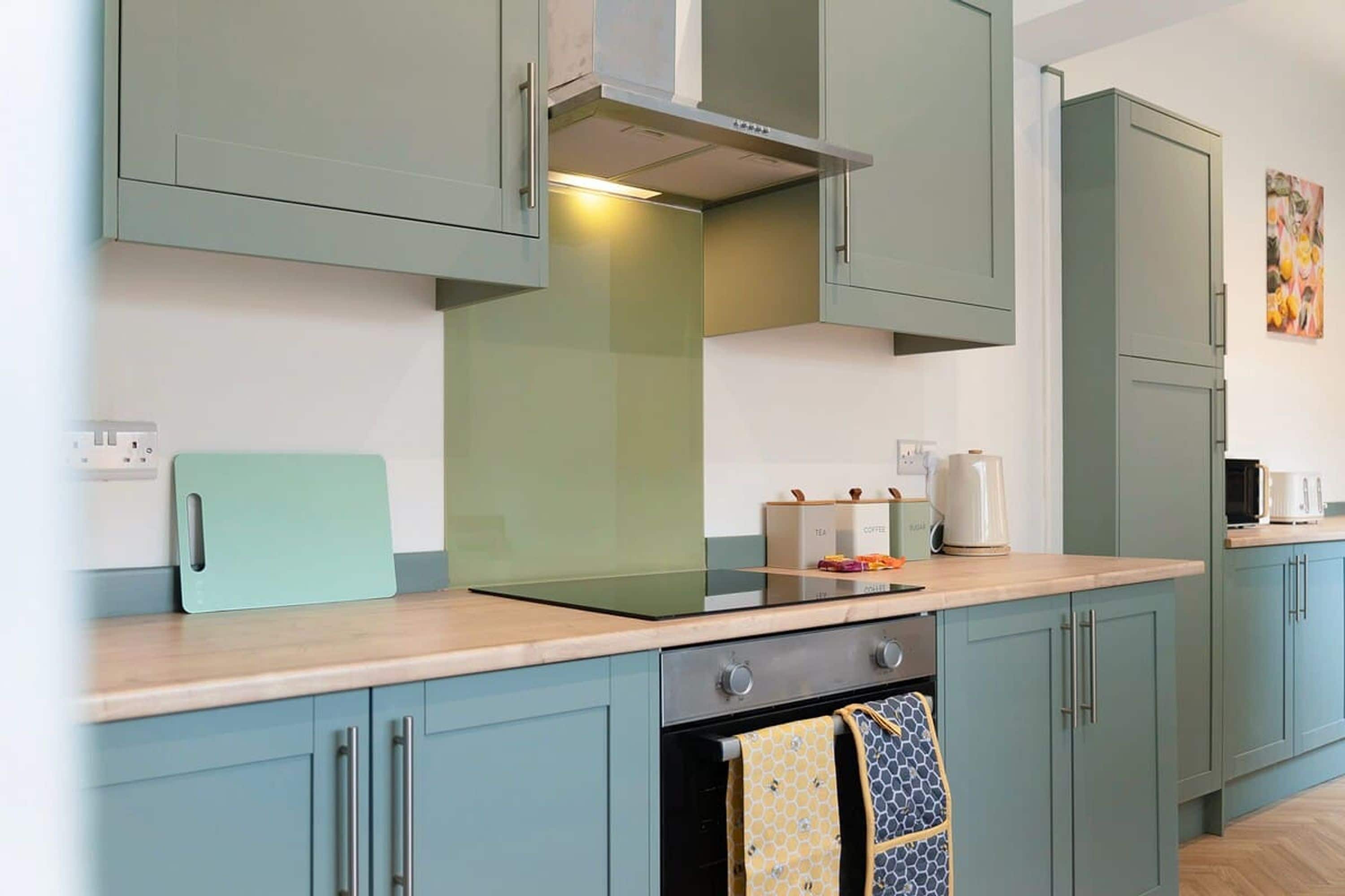 A modern kitchen with teal cabinets, a stainless steel range hood, and a wooden countertop.