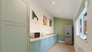Eine kompakte Küche mit Mikrowelle, Toaster und Kühlschrank. Es gibt Schränke und ein Fenster für natürliches Licht.