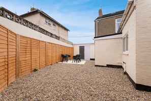 Un cortile residenziale con patio in ghiaia, recinzione in legno e una porta che dà accesso a una casa.