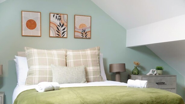 Ein Schlafzimmer mit Bett, Kissen, einem Nachttisch mit Lampe und Wandbildern.