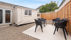 Eine Terrasse mit weißem Boden, einem Holzzaun und mehreren schwarzen Stühlen.