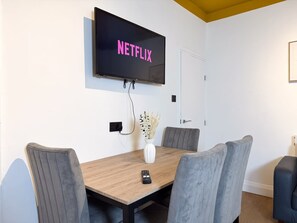A conference room with a wooden table, grey upholstered chairs, a mounted television displaying 'NETFLIX', and a vase with dried plants. - Prime TS1 Location Walk to Shop Uni and Transport (Middlesbrough)