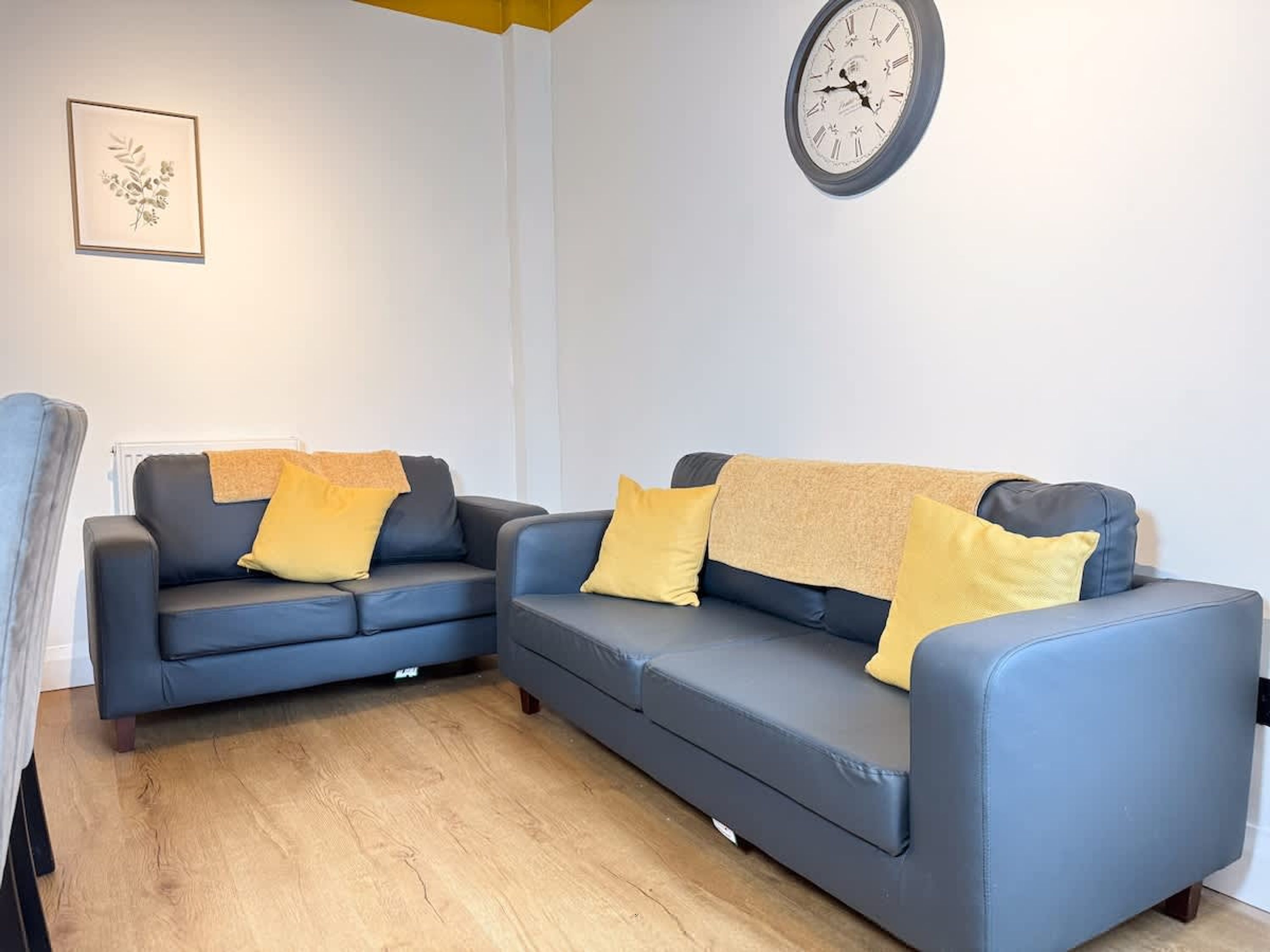 A living room with two sofas, a clock on the wall, and a framed picture.
