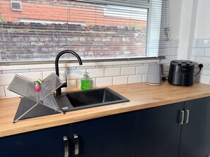Eine Küche mit einem schwarzen Spülbecken, einem Wasserkocher und einer Kaffeemaschine auf der Arbeitsfläche.