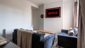 Moderni olohuone, jossa on seinälle asennettu taulutelevisio, sohva, sohvapöytä ja ikkuna, jossa on verhot.