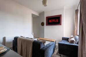 Ein modernes Wohnzimmer mit einem an der Wand montierten Flachbildfernseher, einer Couch, einem Couchtisch und einem Fenster mit Vorhängen.