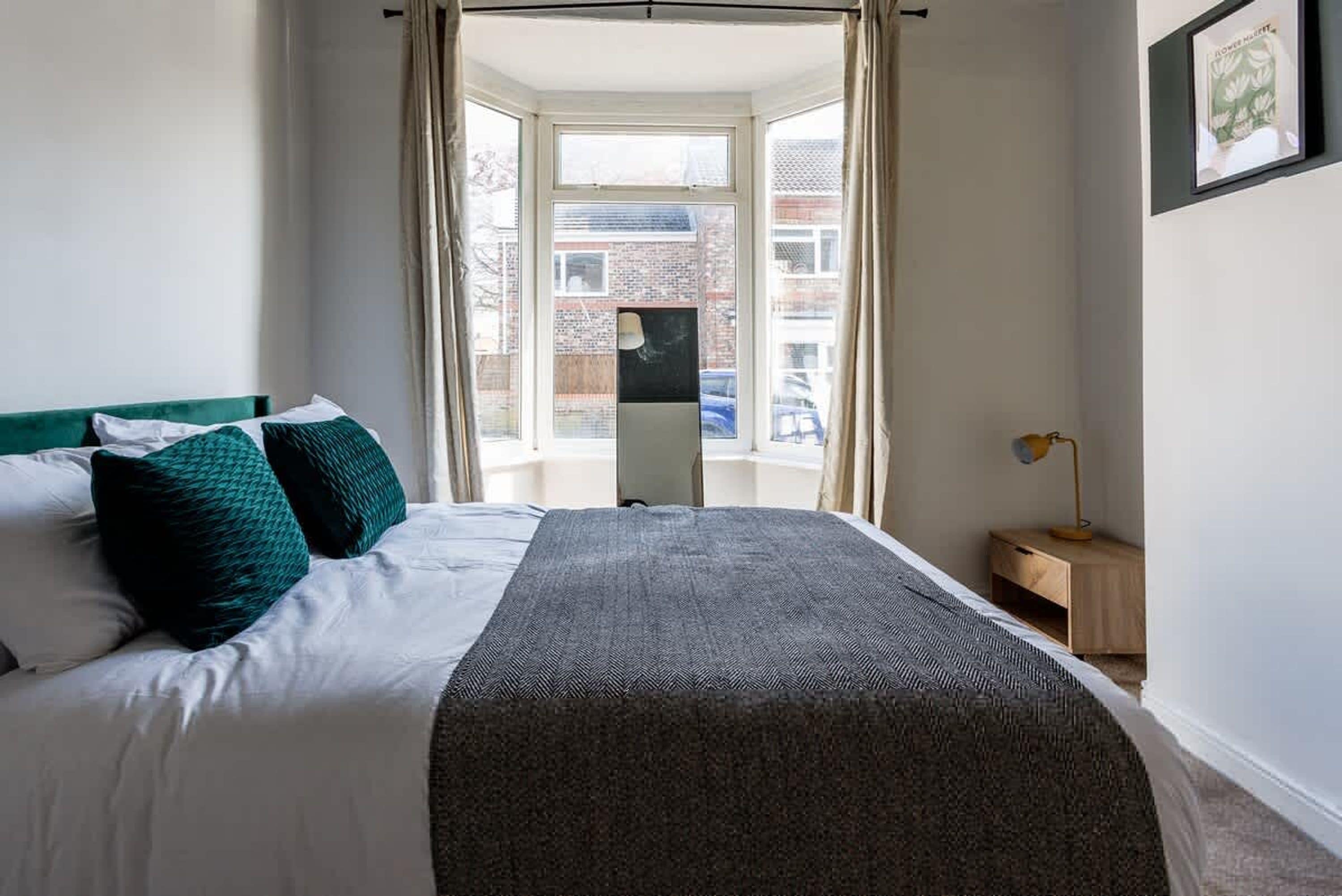 A bedroom with a bed, a nightstand, a lamp, and a window with curtains.