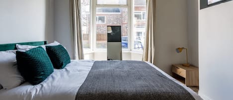 Un dormitorio con una cama, una mesita de noche, una lámpara y un ventanal con cortinas.