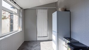 Kapea käytävä, jossa on valkoinen ovi, valkoinen jääkaappi ja roskakori.