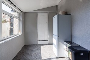 Ein schmaler Flur mit einer weißen Tür, einem weißen Kühlschrank und einem Mülleimer.